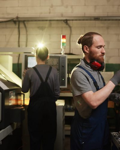 Manual worker in work wear examining the metal details and produced them on the metal factory